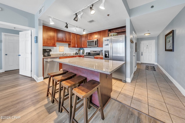 kitchen with light stone counters, stainless steel appliances, a kitchen island, a sink, and visible vents