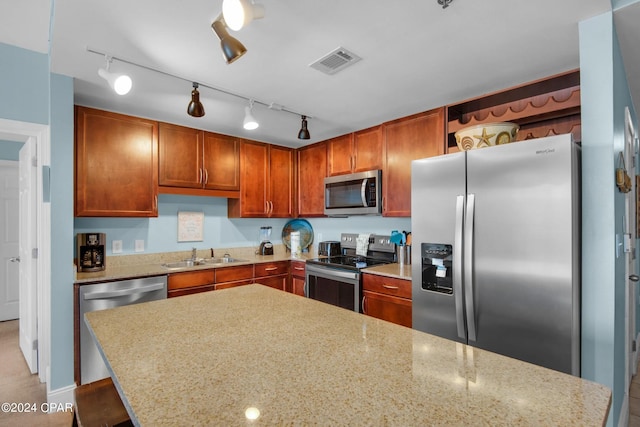 kitchen featuring stainless steel appliances, rail lighting, sink, light stone counters, and a kitchen island