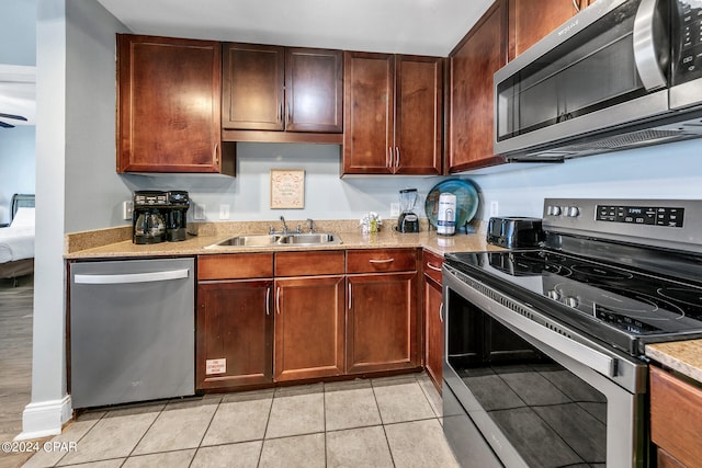 kitchen featuring light tile patterned floors, appliances with stainless steel finishes, light stone counters, and a sink