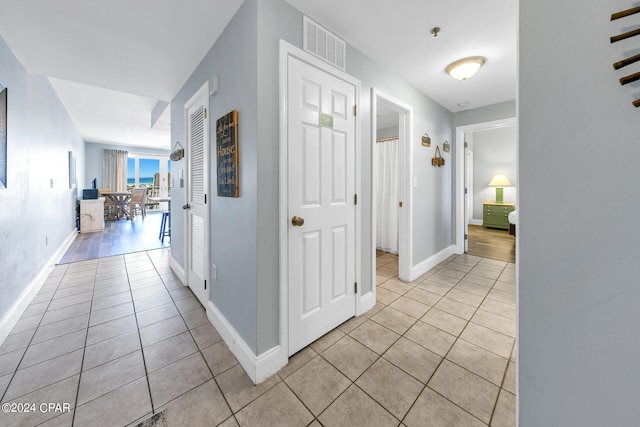 hall featuring light tile patterned floors, visible vents, and baseboards