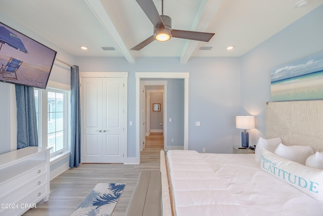 bedroom featuring beamed ceiling, ceiling fan, light wood-type flooring, and a closet