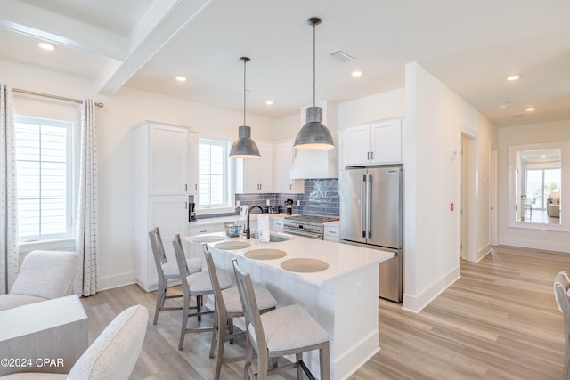 kitchen with decorative light fixtures, tasteful backsplash, premium appliances, a kitchen island with sink, and light wood-type flooring