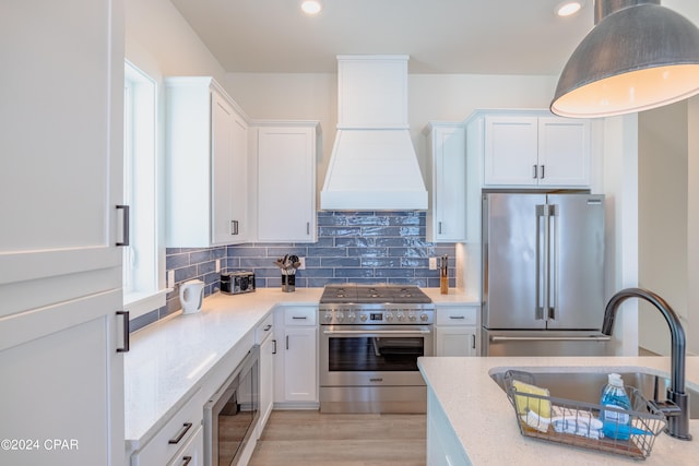 kitchen with backsplash, custom range hood, high quality appliances, white cabinetry, and light wood-type flooring