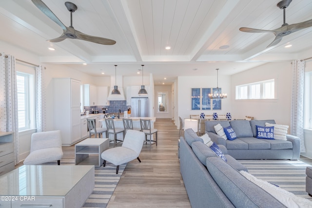 living room featuring ceiling fan with notable chandelier, light hardwood / wood-style flooring, beam ceiling, and sink