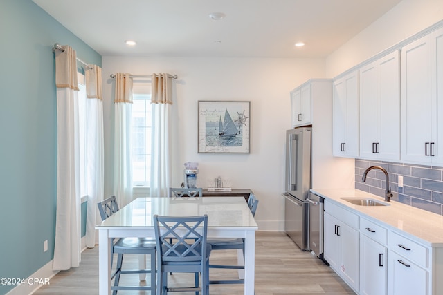 kitchen featuring white cabinets, light hardwood / wood-style flooring, appliances with stainless steel finishes, sink, and tasteful backsplash