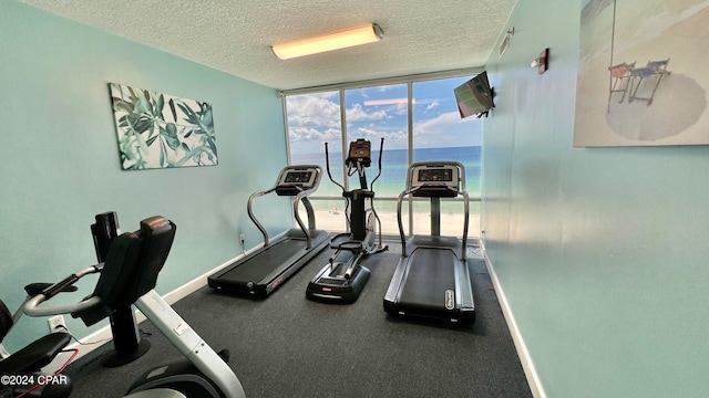 workout room featuring a water view, a textured ceiling, and expansive windows