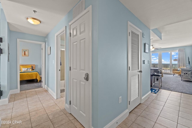 hall with light carpet, visible vents, baseboards, and light tile patterned floors