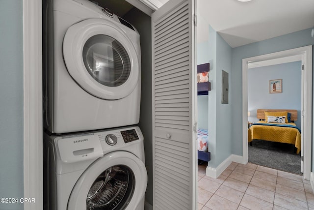 washroom featuring stacked washing maching and dryer, baseboards, light tile patterned floors, and laundry area