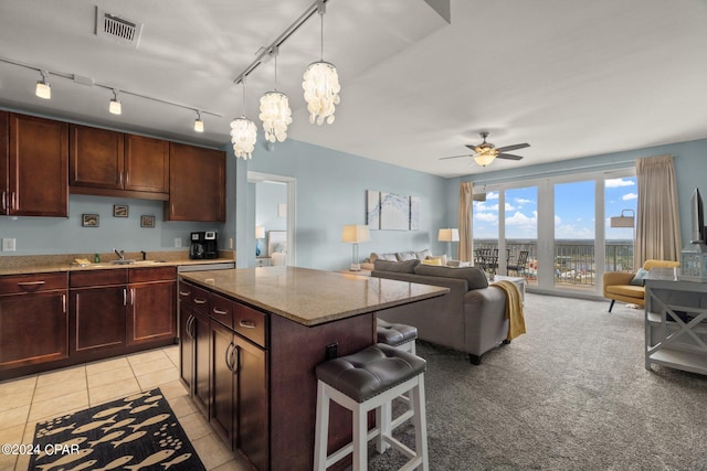 kitchen featuring visible vents, a kitchen island, a breakfast bar, light stone countertops, and a sink