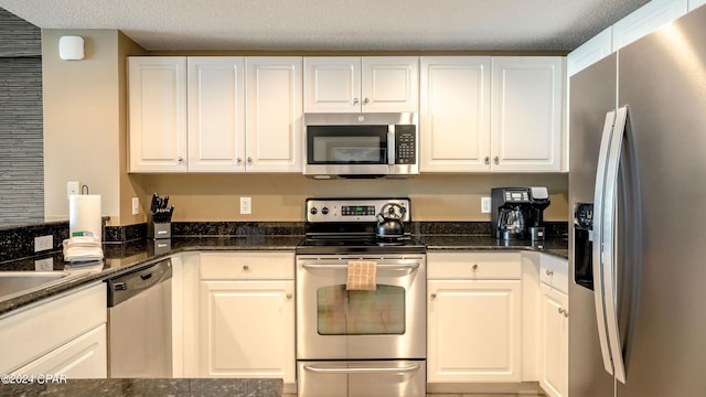 kitchen with white cabinets, stainless steel appliances, and dark stone countertops