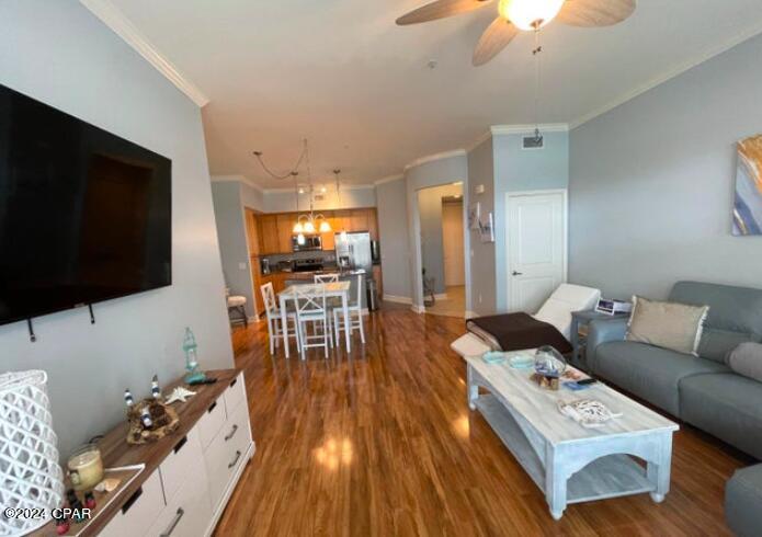 living room featuring ceiling fan with notable chandelier, ornamental molding, and dark hardwood / wood-style floors