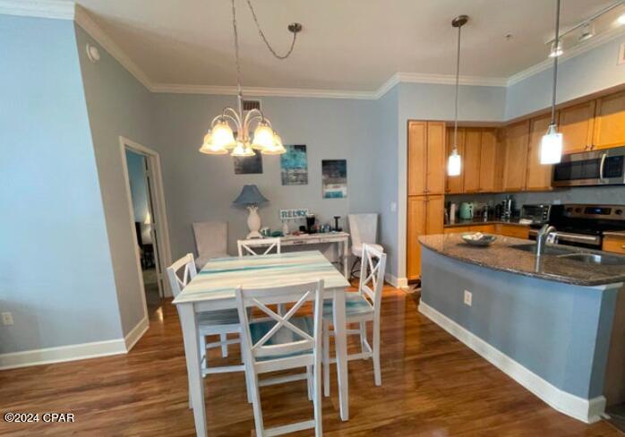 kitchen with pendant lighting, stainless steel appliances, an island with sink, an inviting chandelier, and dark stone countertops