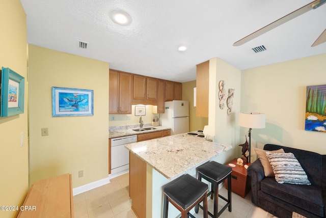 kitchen with white appliances, light stone countertops, kitchen peninsula, a breakfast bar, and sink