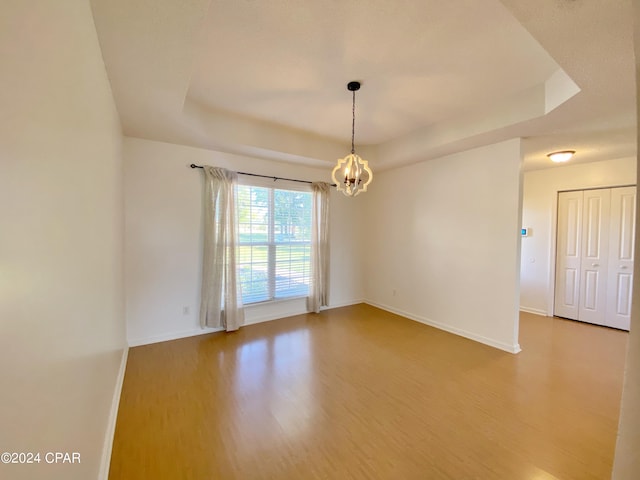 empty room featuring an inviting chandelier, hardwood / wood-style flooring, and a raised ceiling