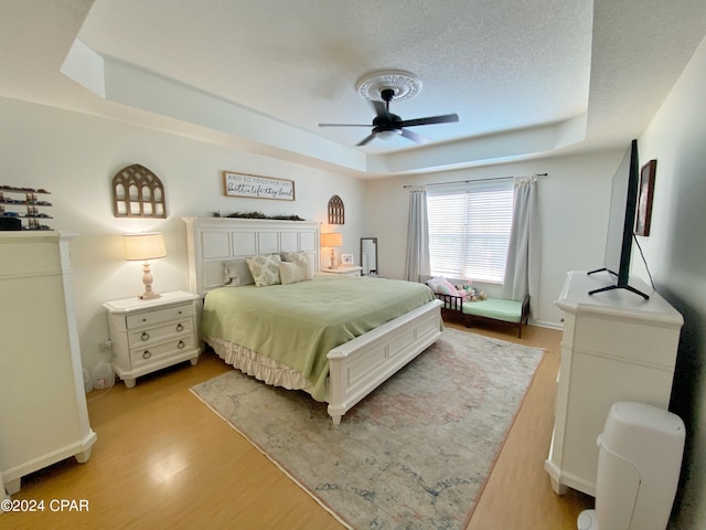 bedroom featuring a textured ceiling, light wood-type flooring, a tray ceiling, and ceiling fan