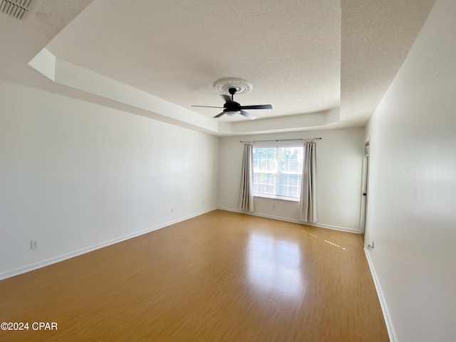 empty room with a raised ceiling, a textured ceiling, light hardwood / wood-style flooring, and ceiling fan