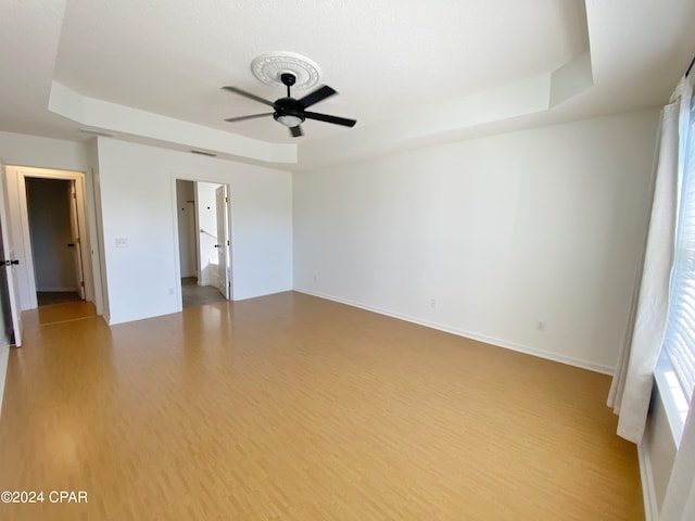 unfurnished room with light hardwood / wood-style floors, a raised ceiling, and ceiling fan