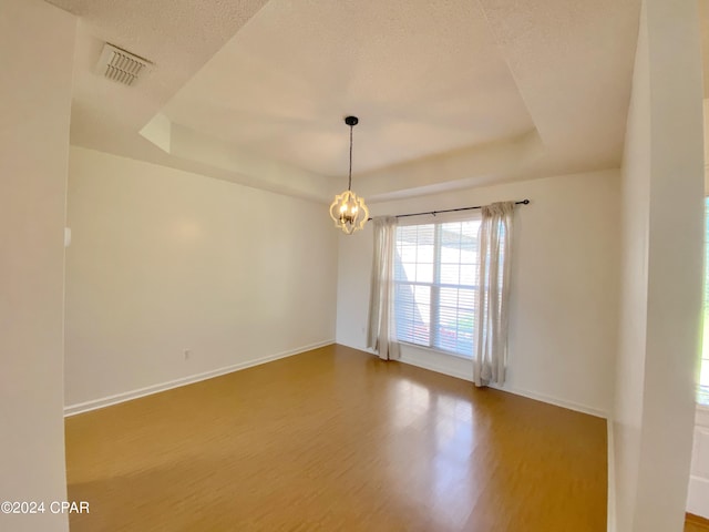 unfurnished room with hardwood / wood-style floors, a textured ceiling, a raised ceiling, and a notable chandelier