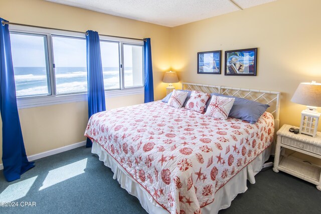 bedroom with a water view, dark colored carpet, and a textured ceiling