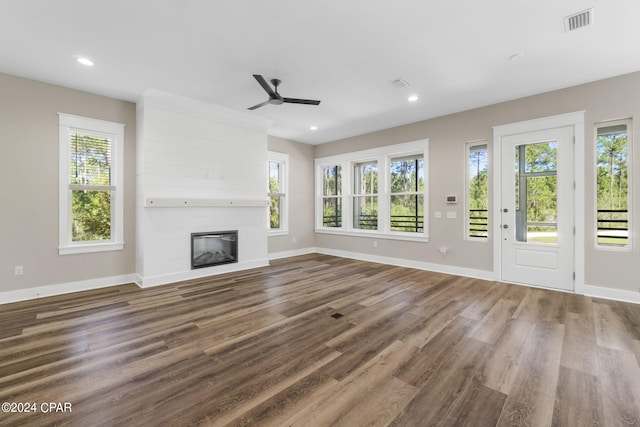 unfurnished living room with wood-type flooring, ceiling fan, a large fireplace, and a healthy amount of sunlight