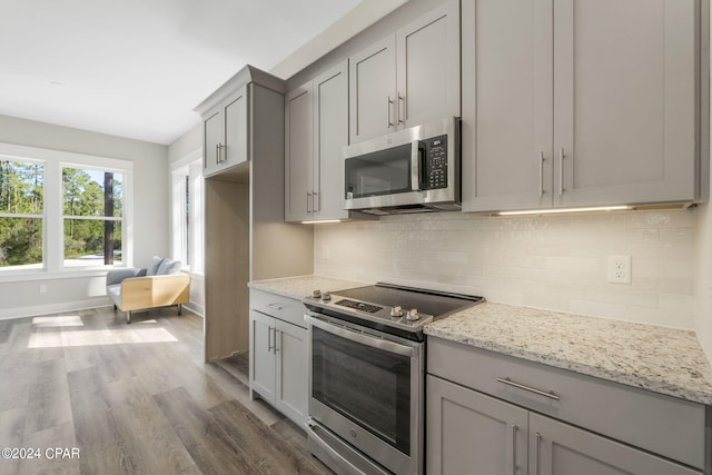 kitchen featuring hardwood / wood-style floors, appliances with stainless steel finishes, backsplash, and light stone countertops