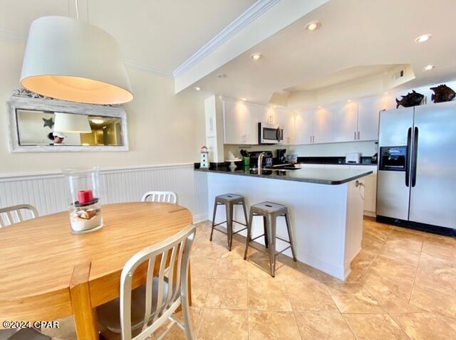 kitchen featuring appliances with stainless steel finishes, light tile floors, white cabinets, ornamental molding, and kitchen peninsula