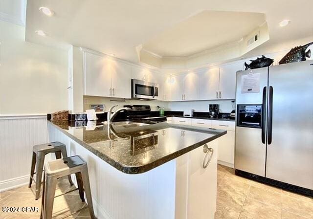 kitchen featuring kitchen peninsula, a breakfast bar area, stainless steel appliances, white cabinetry, and light tile floors