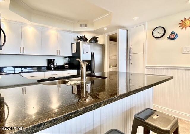 kitchen with a kitchen bar, a raised ceiling, stainless steel fridge, and white cabinetry