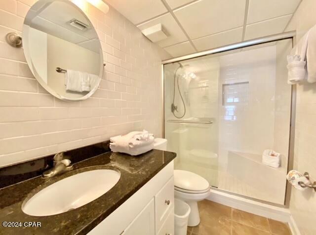 bathroom featuring tile floors, large vanity, a drop ceiling, a shower with shower door, and toilet