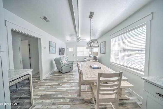 dining room with ceiling fan, light wood-type flooring, lofted ceiling, wine cooler, and a textured ceiling