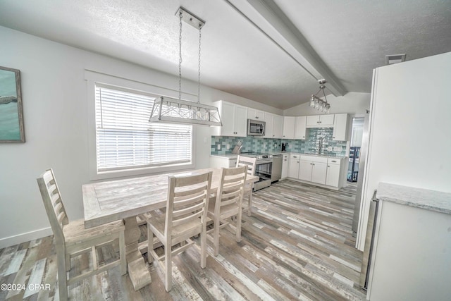 dining room with a textured ceiling, sink, light hardwood / wood-style floors, and lofted ceiling with beams