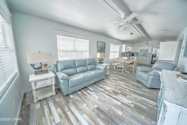 living room featuring ceiling fan, a textured ceiling, light hardwood / wood-style flooring, and lofted ceiling with beams