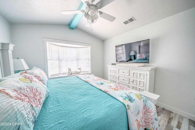 bedroom with ceiling fan, vaulted ceiling with beams, a textured ceiling, and hardwood / wood-style floors