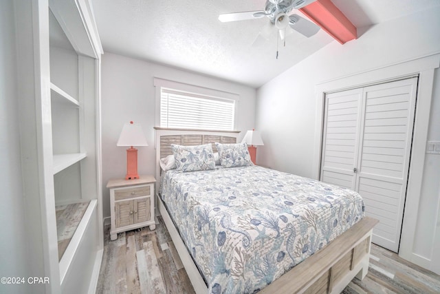 bedroom featuring a textured ceiling, light hardwood / wood-style floors, a closet, lofted ceiling with beams, and ceiling fan