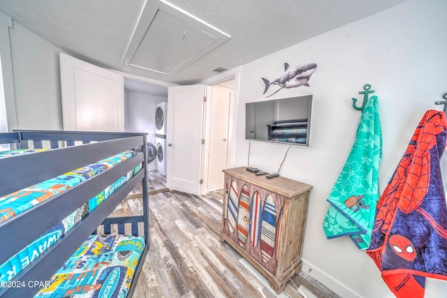 bedroom with stacked washing maching and dryer, a textured ceiling, and hardwood / wood-style flooring