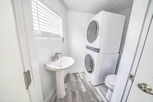 bathroom featuring stacked washing maching and dryer, toilet, hardwood / wood-style floors, and sink