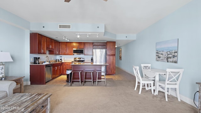 kitchen featuring a center island, stainless steel appliances, a kitchen breakfast bar, track lighting, and light carpet