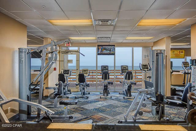 exercise room with a drop ceiling, floor to ceiling windows, and a water view