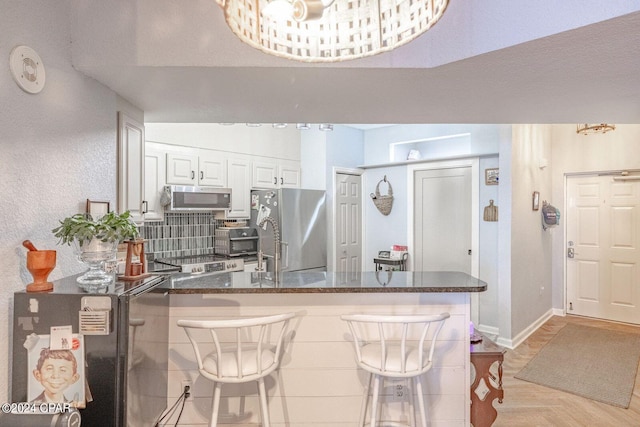 kitchen with light parquet floors, backsplash, stainless steel appliances, white cabinetry, and dark stone countertops