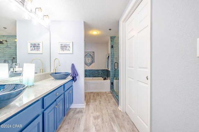 bathroom with vanity with extensive cabinet space, a textured ceiling, shower with separate bathtub, double sink, and wood-type flooring