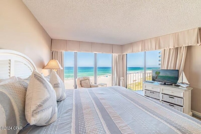 bedroom featuring a view of the beach, a water view, access to outside, and a textured ceiling