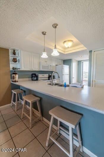 kitchen with a kitchen breakfast bar, white cabinets, white appliances, kitchen peninsula, and a raised ceiling