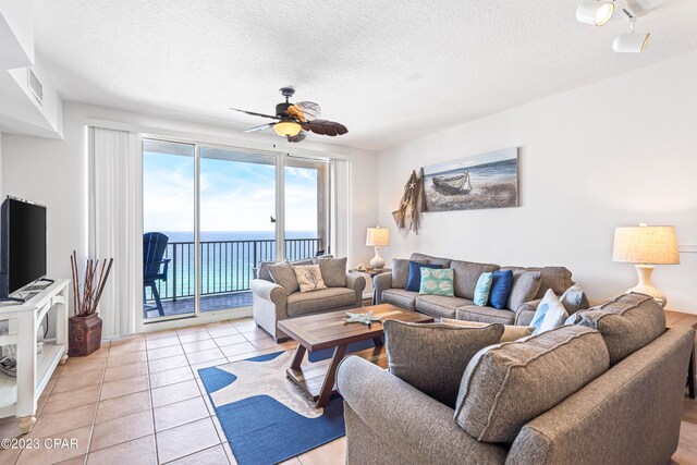 living room featuring ceiling fan, a textured ceiling, light tile patterned floors, and a water view