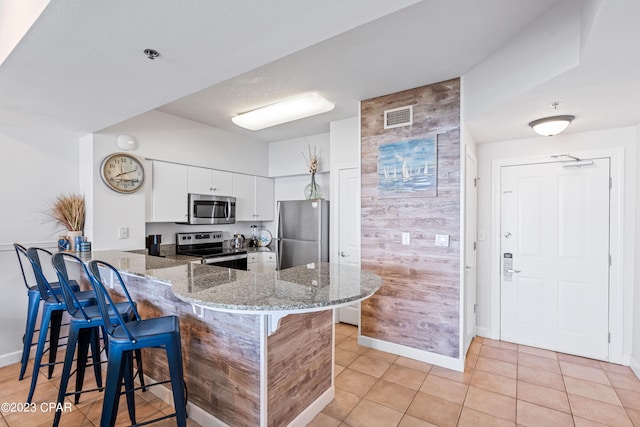 kitchen featuring appliances with stainless steel finishes, white cabinets, kitchen peninsula, light tile patterned floors, and stone counters