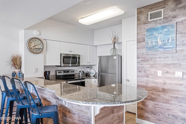 kitchen featuring kitchen peninsula, a kitchen bar, stainless steel appliances, and white cabinets