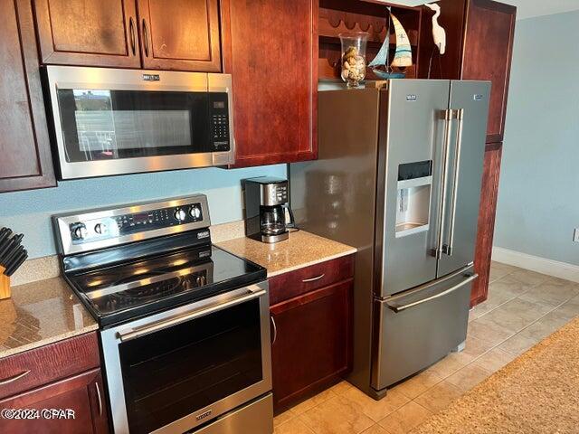 kitchen featuring stainless steel appliances, light tile floors, and light stone counters