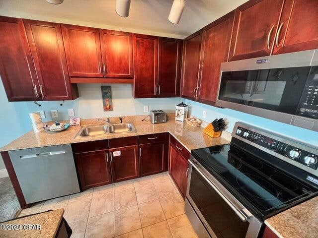 kitchen featuring appliances with stainless steel finishes, ceiling fan, light tile flooring, light stone counters, and sink