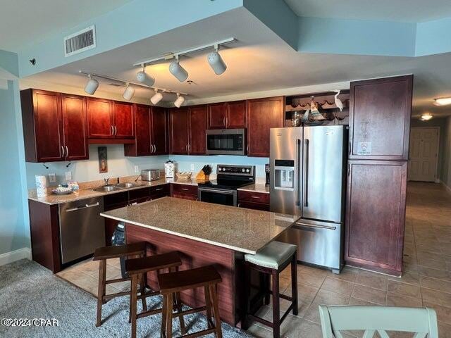 kitchen with light tile flooring, stainless steel appliances, a kitchen bar, a kitchen island, and track lighting