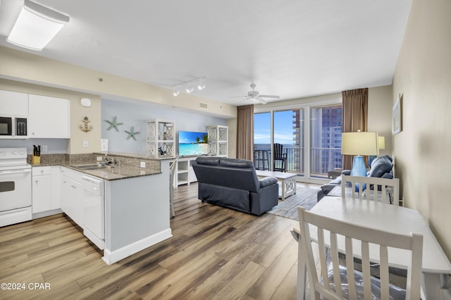 kitchen with sink, kitchen peninsula, white appliances, hardwood / wood-style floors, and white cabinets