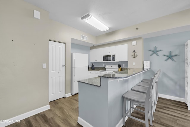 kitchen with white appliances, kitchen peninsula, white cabinets, and a kitchen bar